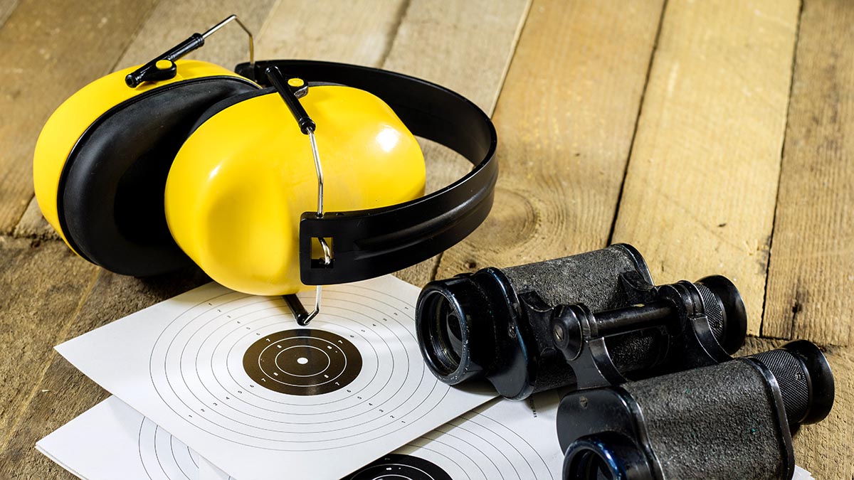 Hörselskydd, kikare och måltavla på en träyta.