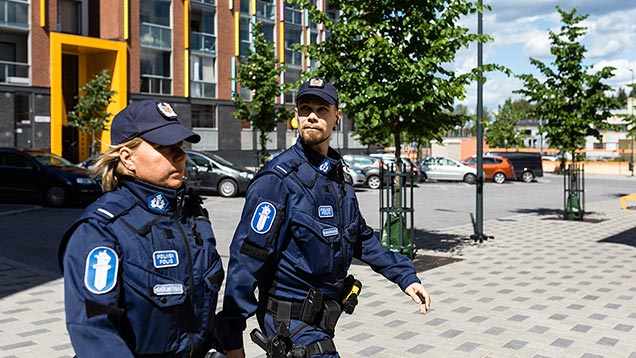 Kaksi poliisia kävelemässä aurinkoisella kaupungin kadulla.